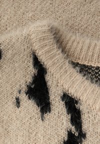 Lähikuva beigeistä pörröisistä neuleista, joissa on musta abstrakti kuvio ja ribattua hihaa, joka peittää kangasta.