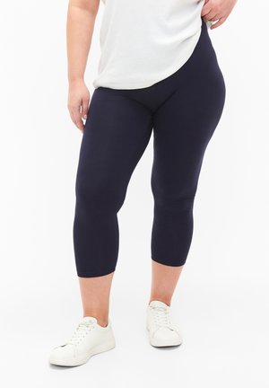 Leggings capri bleu marine en tissu extensible, avec une texture lisse et une coupe ajustée, associées à des baskets blanches.
