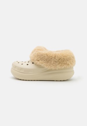 Beige slip-on træsko med ventilationshuller og tyk, blød beige imiteret pelsforing rundt om åbningen, på hvid baggrund.