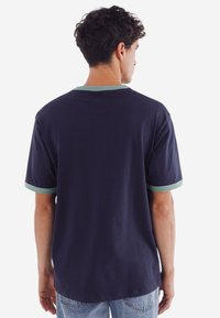 Marinblå t-shirt med ljusgrön ribbad krage och ärmar, tillverkad av mjukt tyg, med avslappnad passform och rundad nederkant.