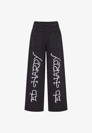 Schwarzweite Jeans mit weitem Bein, großer weißer Schrift an den Seiten, Fünf-Taschen-Design und hoch geschnittenem Bund.