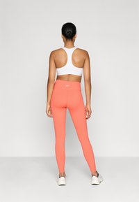 Brasier deportivo blanco con diseño de espalda nadadora combinado con leggings de tiro alto en un brillante color coral; ambos confeccionados en un tejido suave y elástico.
