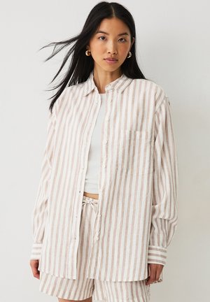 Chemise à carreaux beige clair et blanche, avec une coupe décontractée, détail de poche et manches retroussées. Fabriquée en tissu léger.