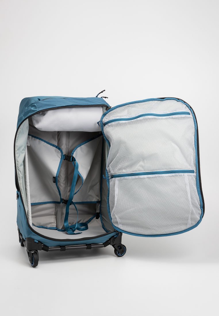 Bolsa de viaje con ruedas en tejido azul y gris; abierta con compartimento de malla, cintas para asegurar el contenido y un interior espacioso.