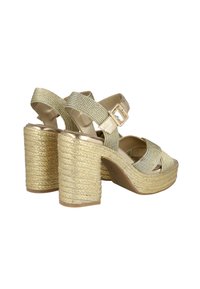 Sandalias de plataforma doradas con pulsera al tobillo, textura trenzada, tacones gruesos de estilo cuerda y un acabado metálico brillante en la suela y las correas.