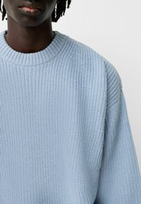 Pull tricoté bleu clair avec un col rond côtelé et une coupe ample, présentant un motif de tissu texturé sur toute la surface.