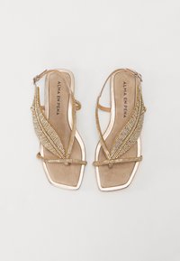 Sandali oro con decorazioni in strass trasparenti, dotati di design a foglia, suola piatta e cinturino alla caviglia. Sottopiedi in suede morbido.