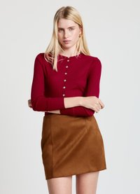 Ribbed red long-sleeve button-up top paired with a brown suede mini skirt. The look features a fitted silhouette and textured fabric.