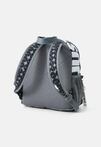 Σακίδιο σε γκρι χρώμα με μαύρο εκτυπωμένο σχέδιο, ρυθμιζόμενες ιμάντες και πλέγμα τσέπης στο πλάι. Διαθέτει χερούλι στην κορυφή και ετικέτα "Just Do It".