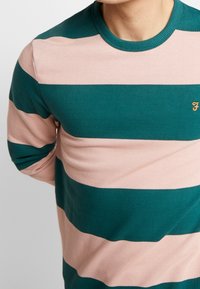 Zielono-różowy sweter w paski z prążkowanym kołnierzykiem, z małym haftowanym logo na piersi. Wykonany z miękkiego materiału dzianinowego.