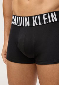 Czarne bokserki wykonane z miękkiego materiału z elastycznym pasem z logo "CALVIN KLEIN" w białym kolorze, ukazujące dopasowany kształt.