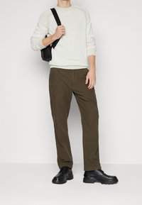 Sweter w kolorze ecru, dzianinowa tkanina z rękawami raglanowymi; brązowe spodnie w kratę o luźnym kroju; czarne buty na grubej podeszwie; czarna torba.