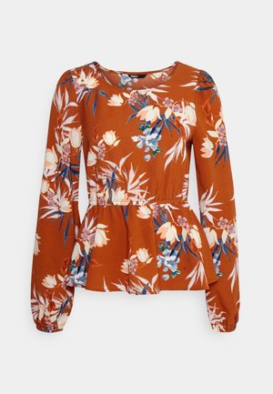 Peplum top in rust orange fabric with floral print in white, blue, and green. Long sleeves with gathered cuffs and a round neckline.