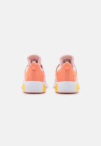 Een paar koraalroze Nike Air Max sneakers gezien vanaf de achterkant, met witte zolen met gele accenten en trekhaakjes op de hielen.