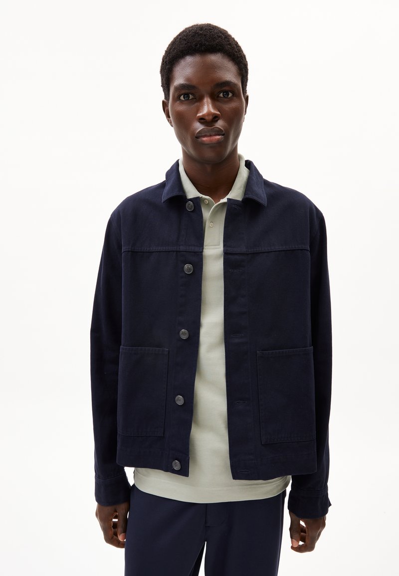 Marineblaue Jacke mit Kragen, vorderem Knopfverschluss und zwei großen Taschen. Der Stoff hat eine glatte, matte Textur.