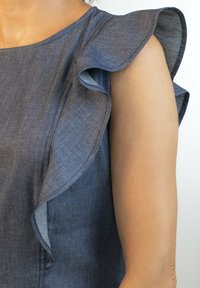 Top azul de chambray con mangas voladas, textura suave y escote redondo. La tela tiene un leve brillo y un acabado suave.