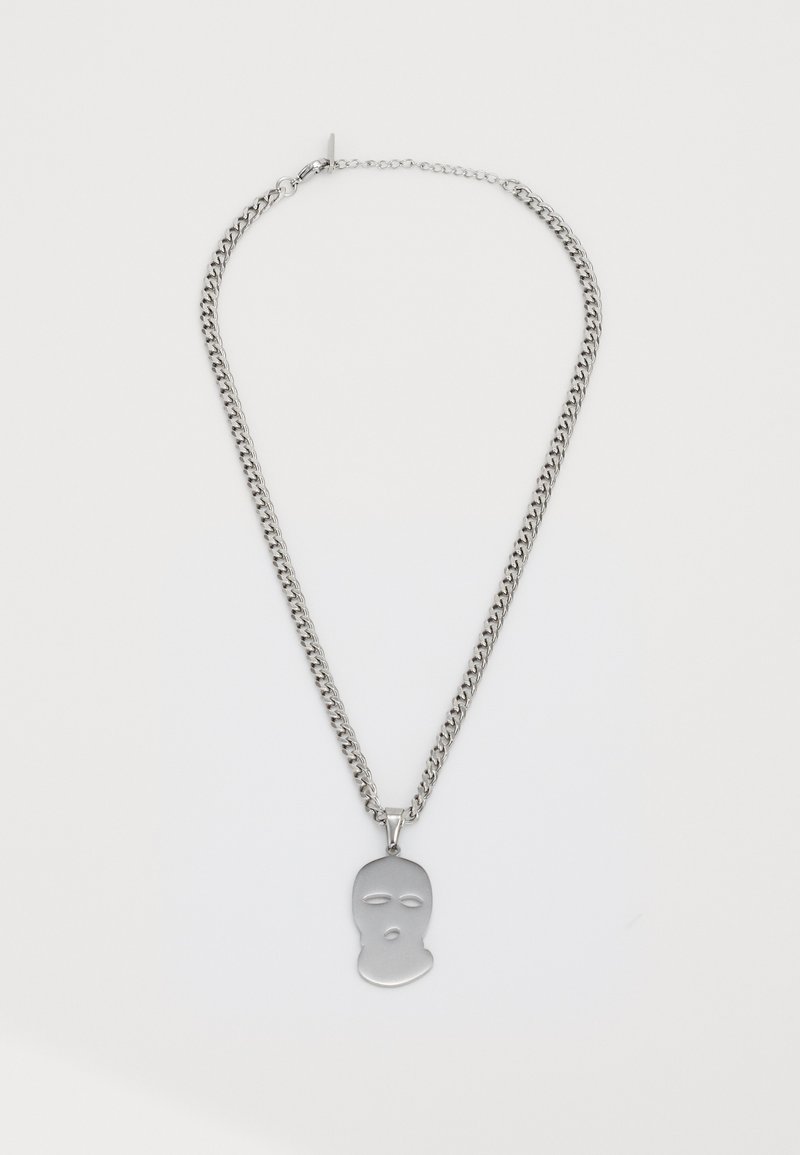Zilveren ketting met een hanger in de vorm van een balaclava-masker, met uitsparingen voor de ogen en mond op een witte achtergrond.