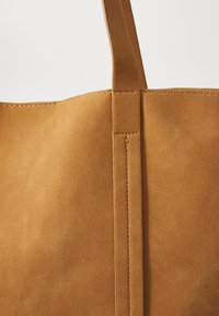 Sac en cuir suédé beige au design minimaliste, texture lisse et couture solide, avec des anses contrastantes et sans embellissements supplémentaires.