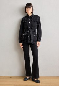 Svart denimjakke med trykknapper, to frontlommer, belted midje, kombinert med utsvingte svarte jeans og spisse svarte leiligheter.