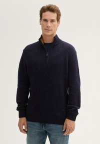 Marineblauw treggingtrui met een ritskraag, geribbelde manchetten en een gestructureerde brei. Bevat multi-kleurige spikkels door de stof.