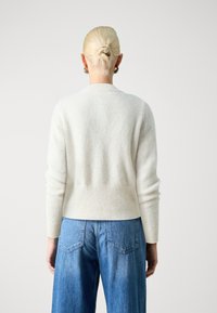 White wool sweater with ribbed texture and crew neck; paired with light blue wide-leg jeans. View from the back, showcasing the outfit's fit.