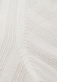 Tela blanca tejida con un patrón texturizado de líneas diagonales y pequeños puntos abiertos, que muestra un suave y sutil brillo.