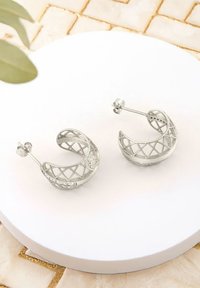 Silvriga hoops örhängen med en öppen geometrisk design, som har en texturerad yta och en säker stiftlåskläpp.