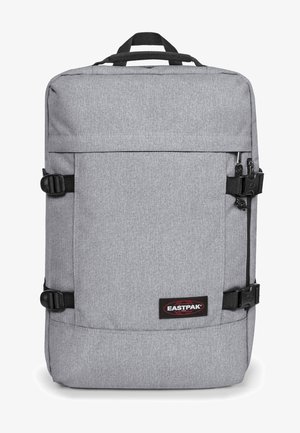 Sac à dos en tissu gris de forme rectangulaire, avec une poche zippée à l'avant, des bretelles noires réglables, des boucles latérales et un patch logo rouge et noir.