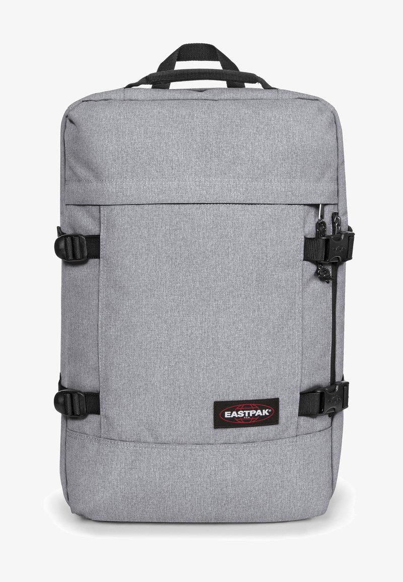 Sac à dos en tissu gris de forme rectangulaire, doté de bretelles noires, de fermetures à boucle et d'un logo Eastpak sur le devant. Texture lisse.