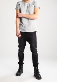Harmaa lyhythihainen T-paita pyöreällä kaula-aukolla, yhdistetty mustiin kuluneisiin slim fit -farkkuihin ja mustiin nauhakenkiin. Yksinkertainen muotoilu, slim fit.