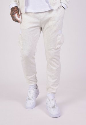 Light grey, herringbone-patterned joggers with two side pockets, tapered ankles, and an elastic waistband, paired with white sneakers.