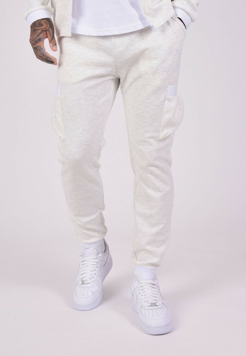 Joggers gris clair à motif chevrons avec deux poches latérales, chevilles fuselées et une taille élastique, associés à des baskets blanches.