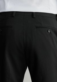 Los pantalones negros de corte entallado presentan una textura suave, un ajuste slim, presillas para cinturón y bolsillos traseros en ángulo con cierres de botón.