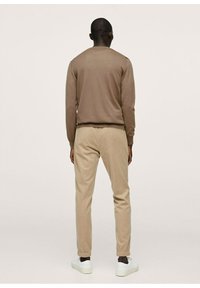 Suéter marrón de manga larga y pantalones tapered beige, ambos fabricados con tela suave, con puños elásticos y zapatillas blancas, vistos desde atrás.