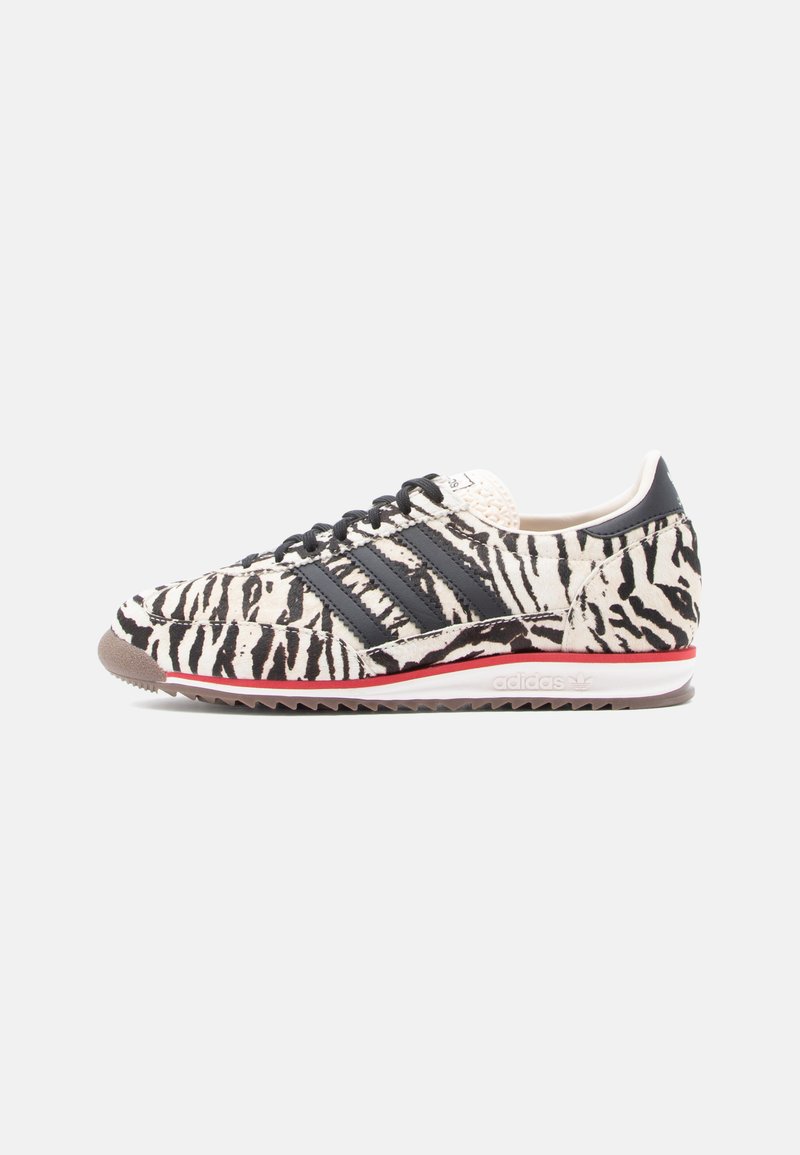 Sneaker with black and white zebra print fabric, three black stripes on the side, and a red accent on the sole. Textured rubber outsole.