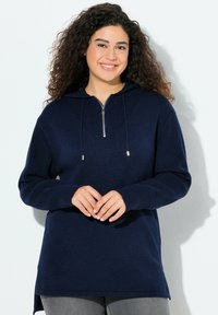 Mörkblå huvtröja med dragkedja i halsen, ribbad textur, långa ärmar och sidofickor. Har ett geometriskt stickat mönster på bröstet.