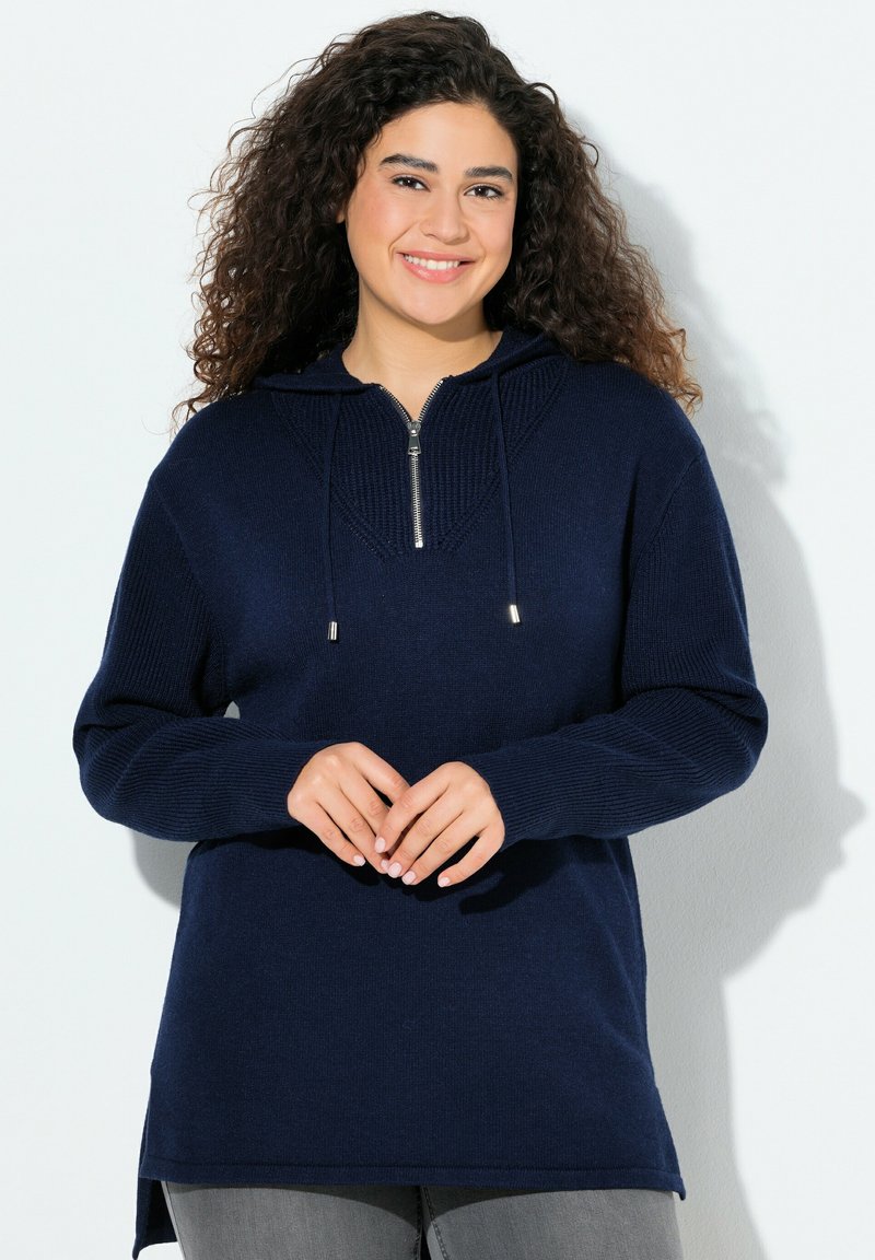 Mörkblå huvtröja med dragkedja i halsen, ribbad textur, långa ärmar och sidofickor. Har ett geometriskt stickat mönster på bröstet.