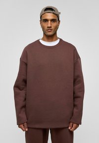 Bruine oversized sweatshirt met een ronde halslijn, voorzien van lange mouwen en stiksel-detailing. Draag over een wit T-shirt.