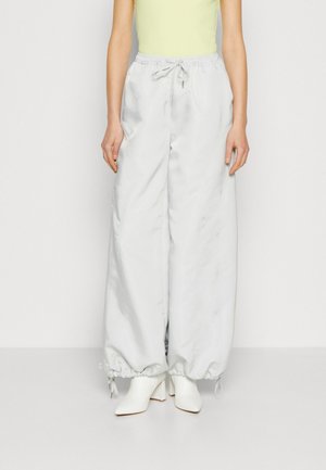 Pantalons larges gris clair avec taille élastique à cordon de serrage, ourlet à revers et texture lisse et brillante. Portés avec des bottines blanches.