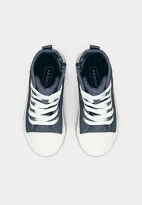 Αθλητικά παπούτσια high-top με επάνω μέρος από σκουρόχρωμο γκρι τζιν, λευκό λαστιχένιο κάλυμμα στα δάχτυλα και σόλα. Διαθέτουν λευκά κορδόνια και μικρές μπλε λεπτομέρειες κοντά στον αστράγαλο.