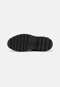 Semelle en caoutchouc noir de sneaker avec de fortes rainures et le logo en relief "CALVIN KLEIN JEANS". Surface texturée pour l'adhérence et la durabilité.