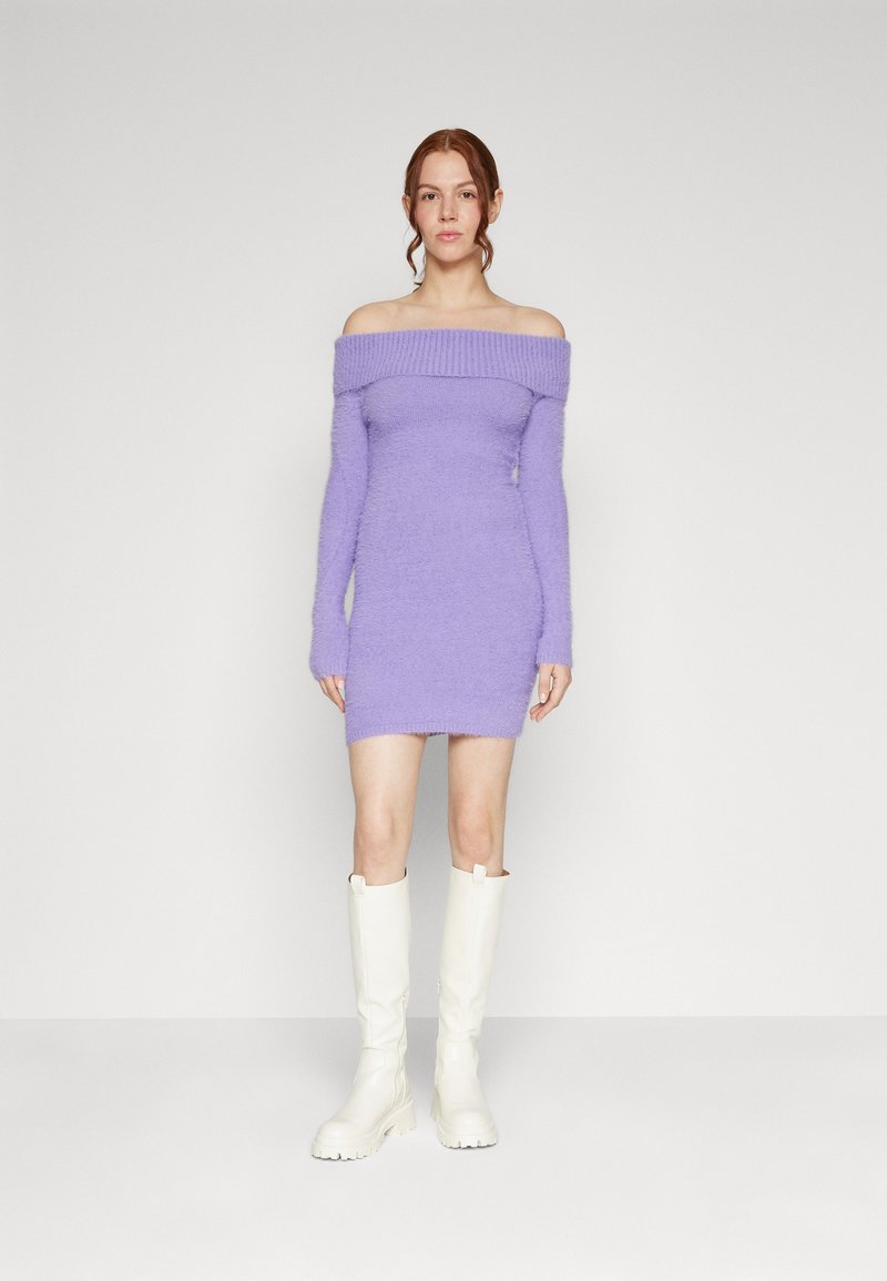 Lila Off-Shoulder-Kleid mit langen Ärmeln, aus flauschigem Material; kombiniert mit weißen Kniestrümpfen. Glatte Textur, figurbetonter Schnitt.