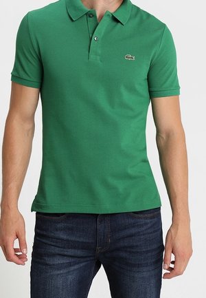 Grünes Poloshirt aus Baumwolle mit klassischem Kragen, kurzen Ärmeln und einem kleinen, bestickten Logo auf der linken Brust, getragen zu blauen Jeans.