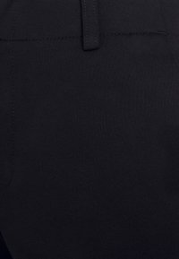 Gros plan sur un pantalon en tissu noir mettant l'accent sur la taille, les passants de ceinture et les détails de couture des poches.