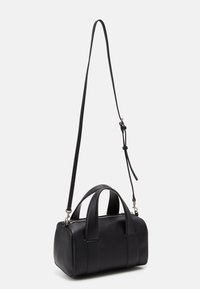 Petit sac à main en cuir noir avec doubles poignées et une longue bandoulière réglable, présenté sur un fond clair uni.