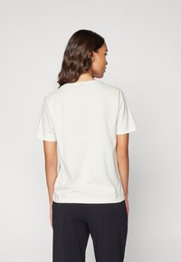 Cream-colored cotton t-shirt featuring a crew neck and short sleeves, visible stitching, and a relaxed fit. Background is gray.