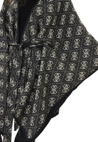 Poncho lavorato a maglia in nero e grigio, con un motivo di logo ripetuto. Ha una cintura per la chiusura e una sensazione morbida e texturizzata.
