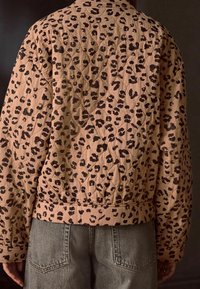 Pikowana kurtka w jasnobeżowym kolorze z czarnym nadrukiem w cętki lamparta, z prążkowanym dołem i mankietami oraz teksturowaną tkaniną dla uzyskania wymiaru.