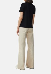 T-shirt noir à manches courtes associé à un pantalon large beige clair. La tenue présente une coupe décontractée et une texture unie. Les chaussures sont de couleur claire.