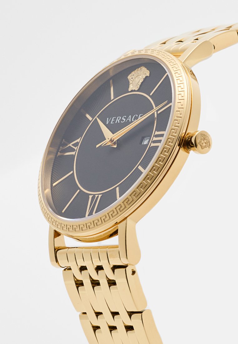 Gouden horloge met een zwarte wijzerplaat, Romeinse cijfermarkeringen, datumaanduiding en schakelschakelarmband. Bevat het Medusa-logo nabij de kroon.